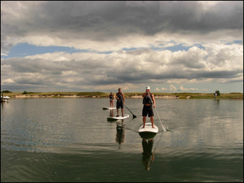 Three people doing stand up and paddle on Cape Cod water.